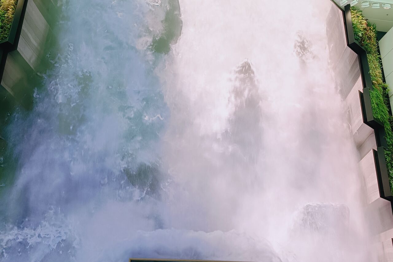 in der Abflughalle schießt ein Riesenwasserfall die Wand lang runter, ...